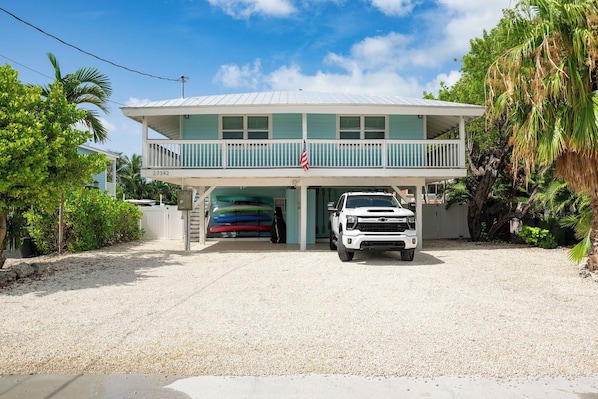 A two-story building with a covered garage, a white pickup truck parked in front, and a row of colorful kayaks inside the garage.