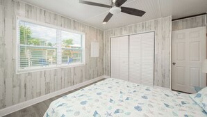 Quarto com cama, ventoinha no teto, janela com persianas e guarda-roupa.