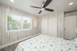 A bedroom with a bed, a ceiling fan, a window with blinds, and a wardrobe.
