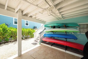 A covered outdoor area with a staircase leading to a house, a row of kayaks, and a satellite dish on the house.