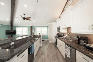 Una cocina moderna con armarios blancos, encimeras de granito y un ventilador de techo.