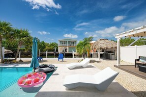 Un espace piscine avec des chaises longues, un grand flotteur en forme de fraise et une maison en arrière-plan.