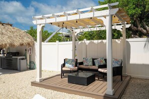 Un espacio de estar al aire libre techado con una pérgola, una parrilla y una estructura de techo de paja.