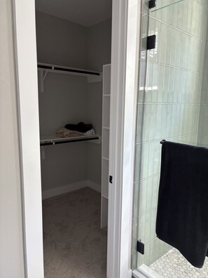 A bathroom with a glass shower enclosure, a towel hanging on the door, and a shelf with folded towels.