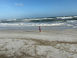 A beach with waves and a child walking on the sand. - 3-bedroom condo in Navarre Beach with Golfcart (Navarre)