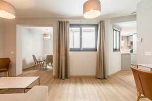 Ein moderner, hell eingerichteter Raum mit Essbereich, einer Küche und einem großen Fenster mit Vorhängen.