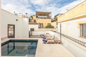 Ein Pool auf dem Dach mit Liegestühlen, einer Glasbrüstung und Blick auf die Nachgebäud