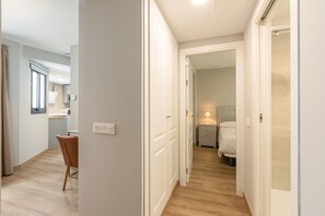 A hotel corridor with a wooden floor, a dining area with a chair and table, and a bedroom with a bed and nightstand. - B2 Apartment with Cathedral Views – City Center & Pool (Seville)