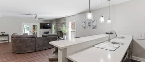 Une cuisine moderne avec un plan de travail blanc, un évier en acier inoxydable et des luminaires suspendus.