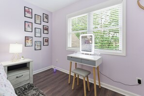 A room with a desk, a chair, a lamp, a bed, and a window with blinds.