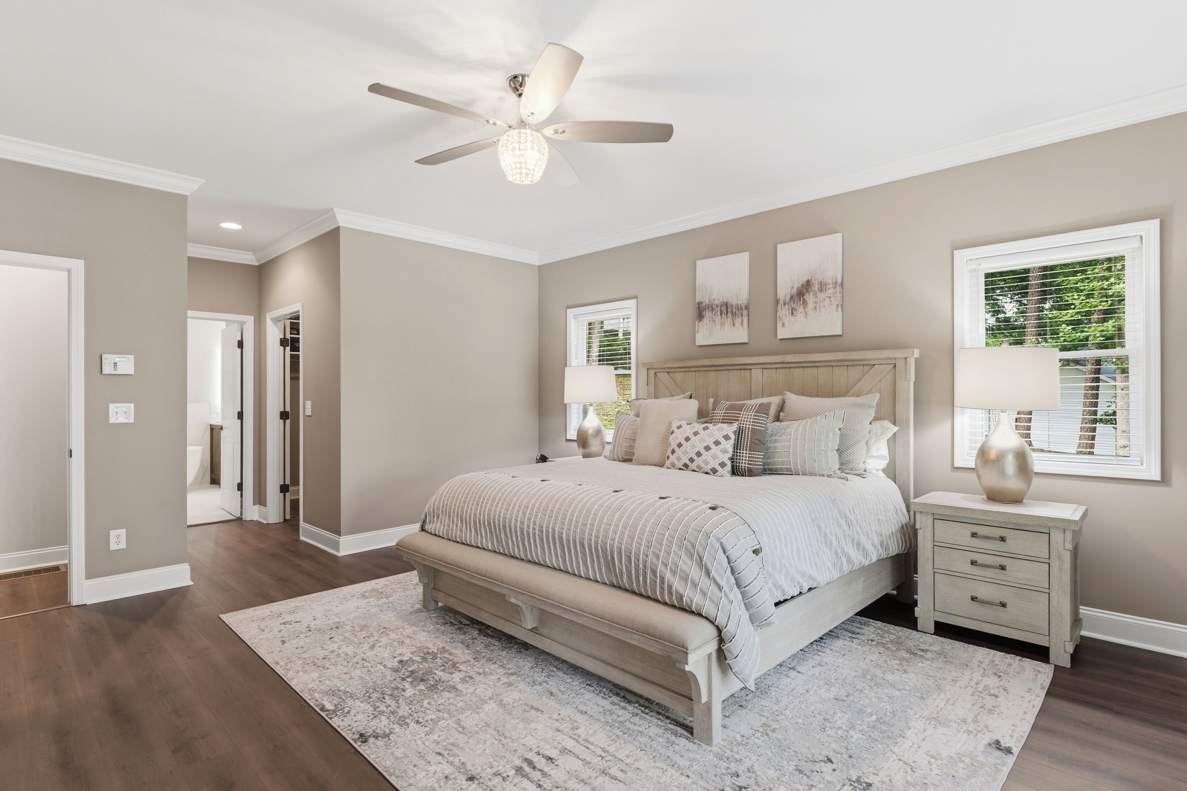 A bedroom with a large bed, bedside tables, a ceiling fan, and artwork on the walls.