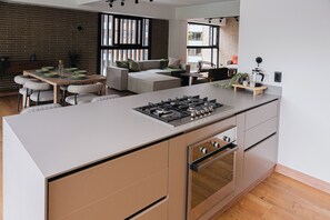 A modern kitchen with a central island, built-in oven, and a dining area with a sofa and chairs. - Altitud Medellín View Living (Medellín)