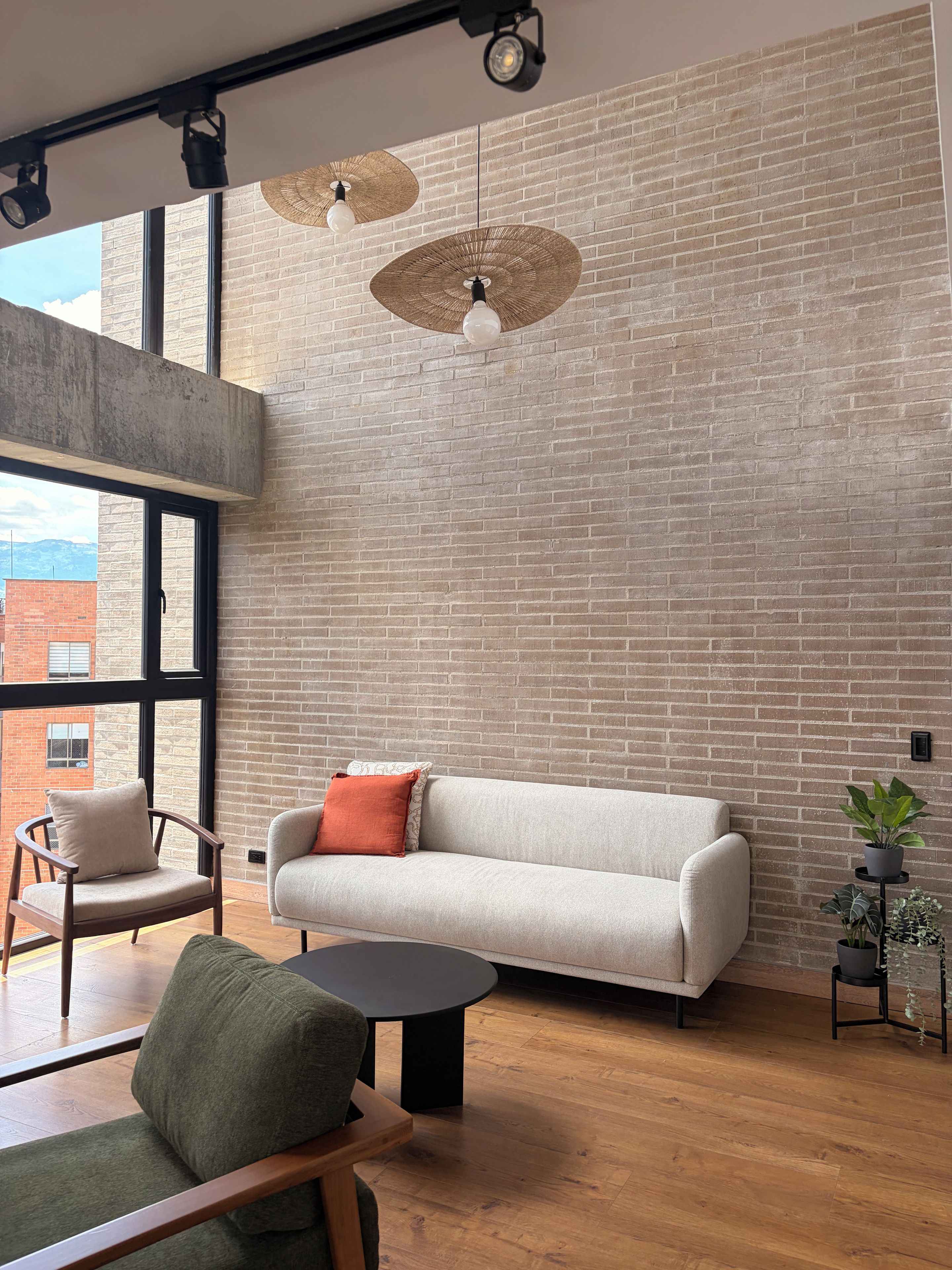 Een moderne woonkamer met een bakstenen muur, een bank, een fauteuil, een salontafel en hanglampen.