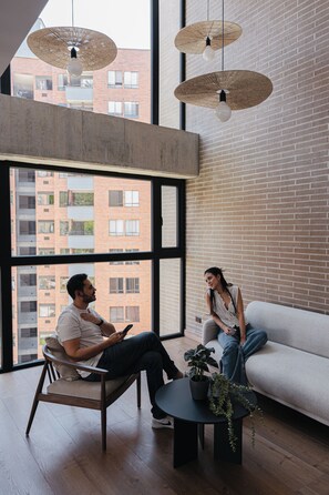 Un interior moderno con un ventanal grande, un sofá, una mesa de centro con una planta y luminarias colgantes.