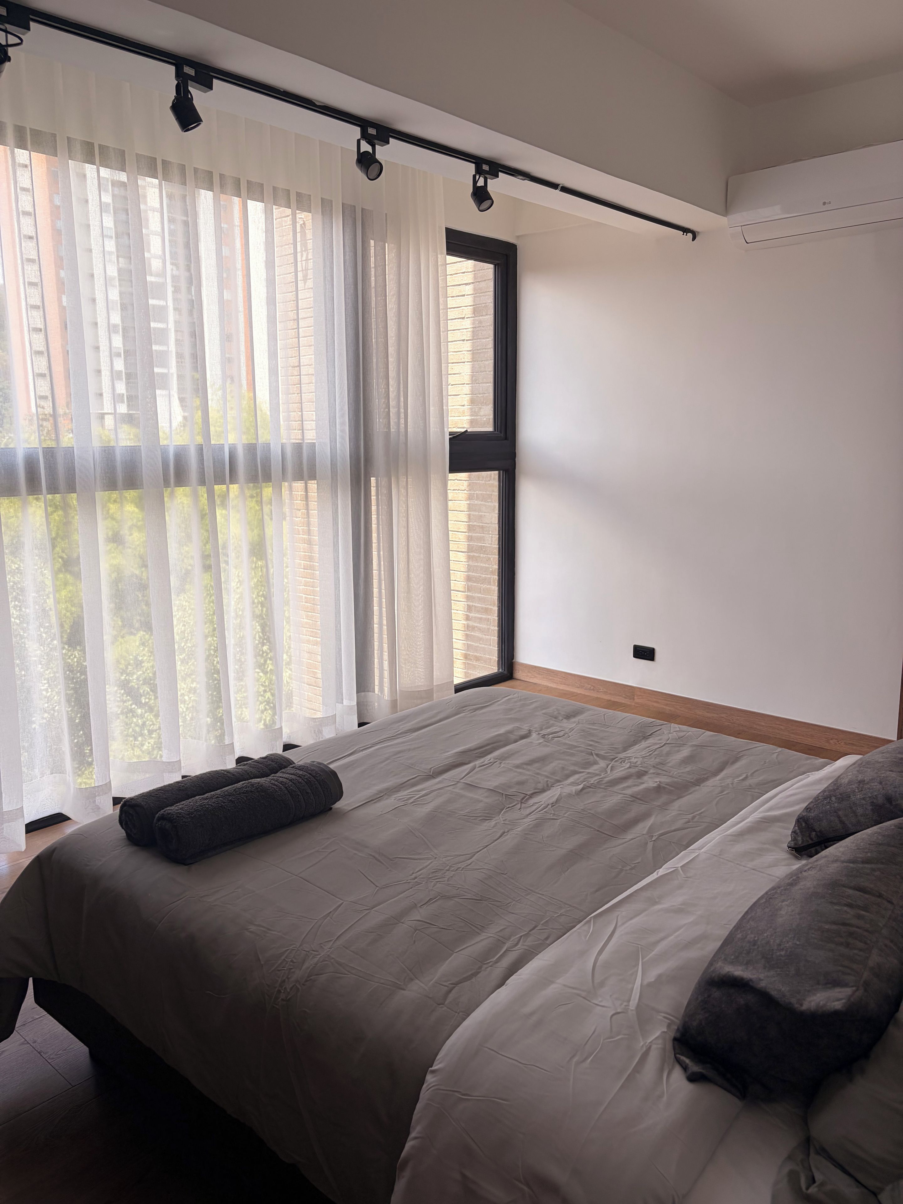Camera da letto con un letto grande, tende leggere e vista sugli edifici esterni.