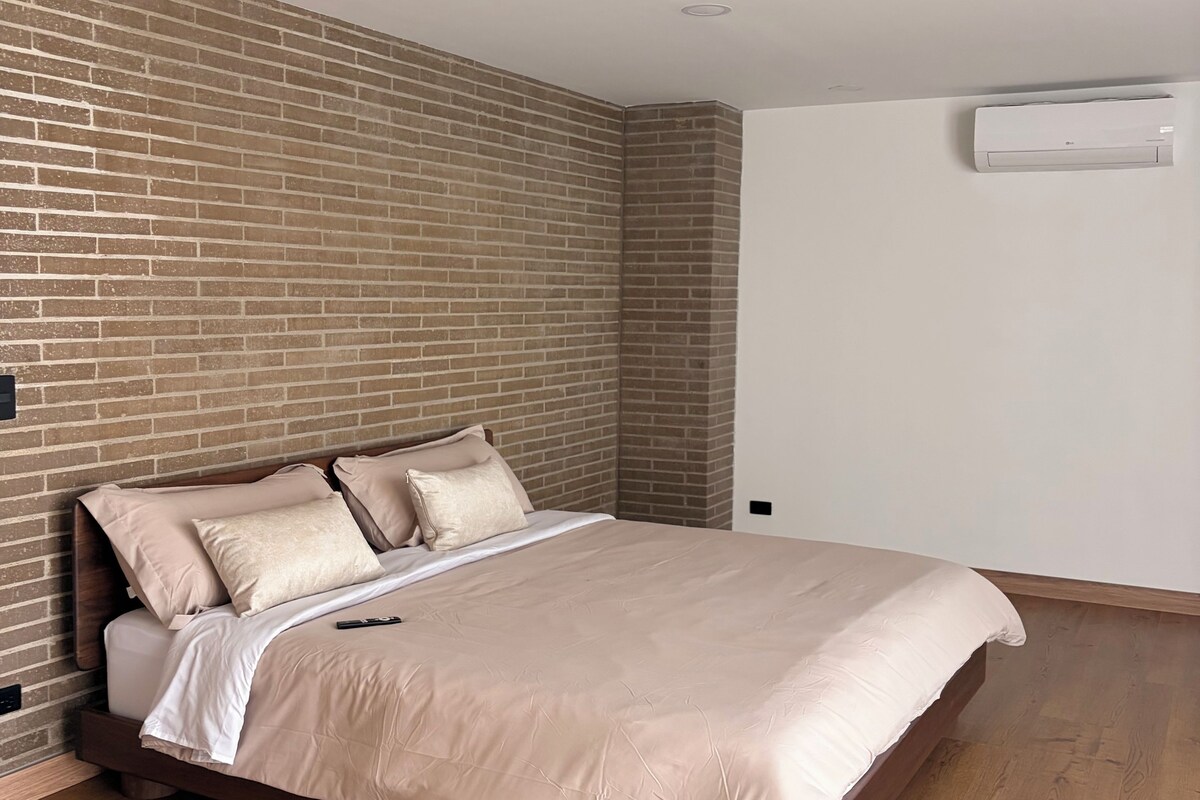 Un dormitorio con pared de ladrillo, estructura de cama de madera y unidad de aire acondicionado blanca.