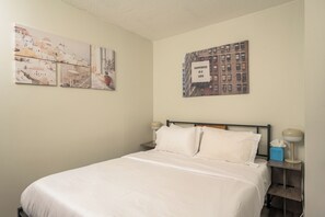 Una habitación de hotel con una cama, una mesita de noche y dos cuadros colgados en la pared.