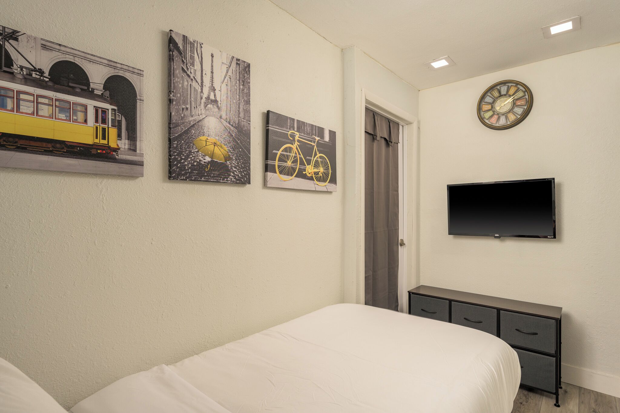 A bedroom with a bed, a dresser, a television, and three framed pictures on the wall.