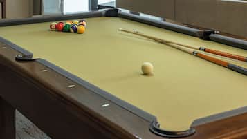 A pool table with balls and cues, a sofa in the background, and a window.