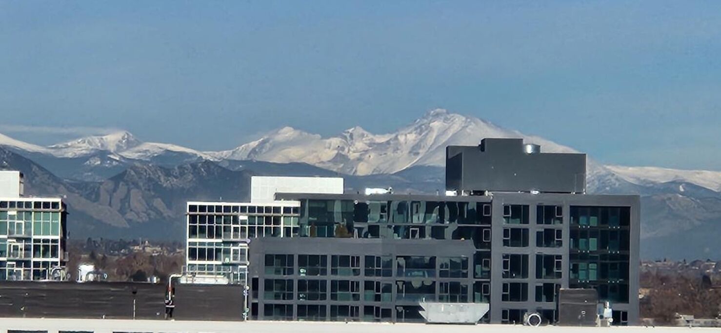 A modern building with multiple floors and large windows, set against a backdrop of snow-capped mountains.