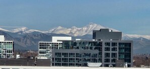 Un edificio moderno con varios pisos y grandes ventanales, con montañas nevadas al fondo.