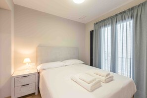 Une chambre d’hôtel avec un lit, une table de chevet, une lampe et une fenêtre avec des rideaux.