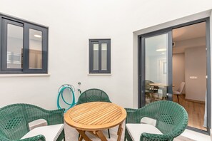 Ein Zimmer mit einem runden Holztisch, zwei grünen Korbstühlen, einem Fenster und einer Tür zu einem anderen Raum.