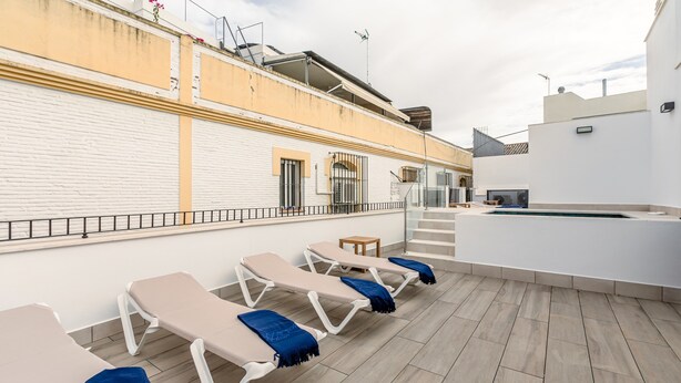Una terrazza sul tetto con lettini, una piscina e un edificio bianco con facciata in mattoni.