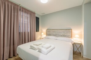 Ein Hotelzimmer mit einem großen Bett, zwei Nachttischlampen, einem Blattmuster-Kopfende und einem Fenster mit Vorhängen.