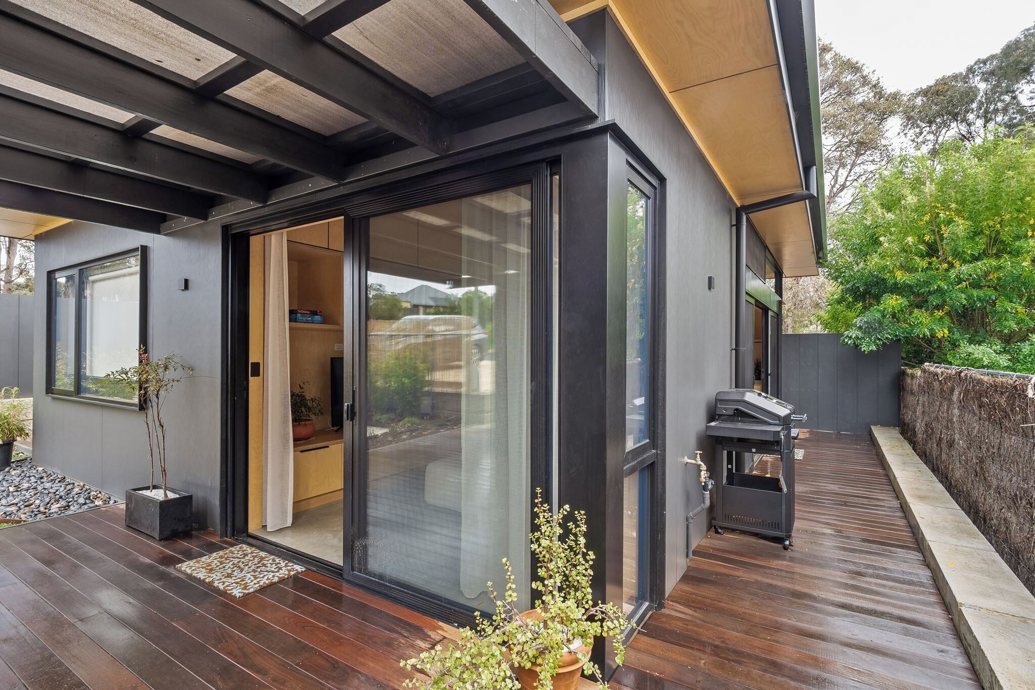 A modern house with a sliding glass door entrance, a wooden deck, and a barbecue area.