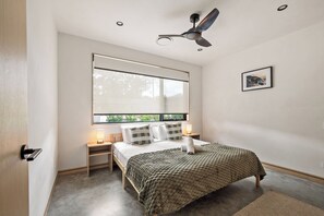 A bedroom with a bed, bedside tables, a ceiling fan, a window with a view, and a framed picture on the wall. - House Kayu - A unique home in the heart of Margaret River (Margaret River)