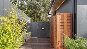 Eine Holzterrasse führt zu einer dunkel gefärbten Wand mit einer kleinen Sitzecke und einer hängenden Lampe.