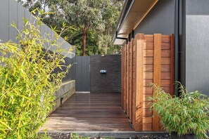 A wooden deck leading to a dark-colored wall with a small seating area and a hanging light fixture. - House Kayu - A unique home in the heart of Margaret River (Margaret River)