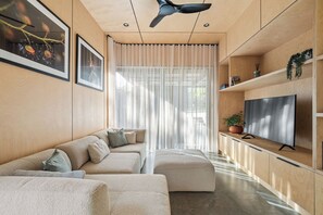 Ein modernes Wohnzimmer mit Sofa, Hocker, Fernseher und Deckenventilator.