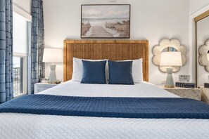 Een hotelkamer met een groot bed, een houten hoofdbord, twee nachtkastjes met lampen, een schilderij boven het bed en uitzicht op het omliggende landschap.