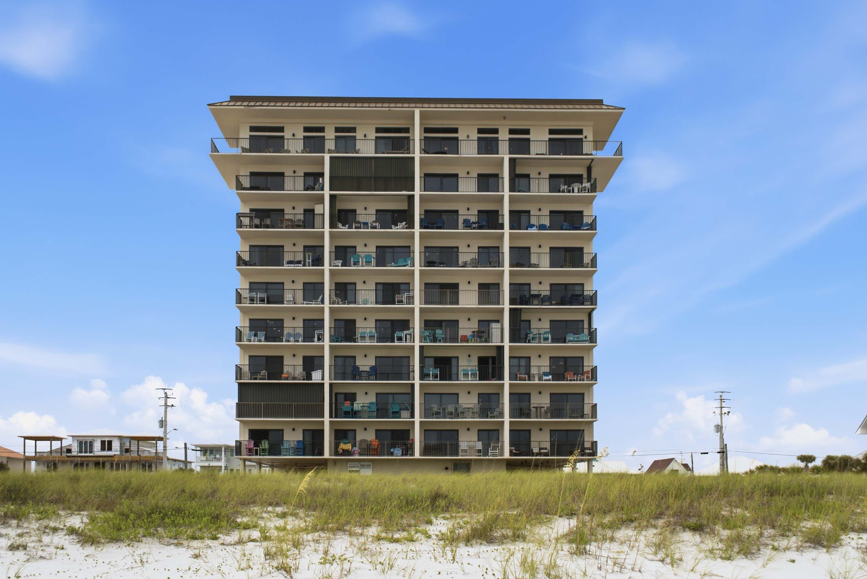 Un hôtel à plusieurs étages, doté de balcons, situé près d’une plage bordée de dunes de sable.