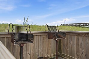 Een houten terras met twee metalen barbecues en een houten omheining.