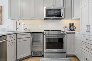 A modern kitchen with stainless steel appliances, white cabinetry, and a tiled backsplash. - Snowbirds Welcome • Gulf Front • Full Kitchen • Elevator • Sundunes 144 (Navarre)
