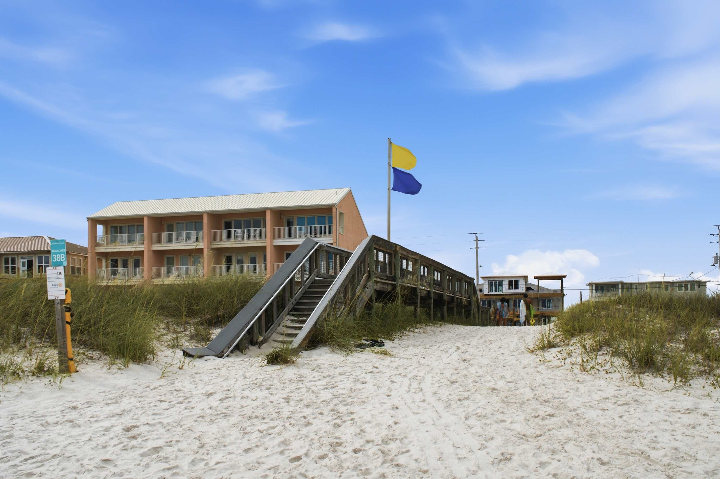 Un bâtiment situé en bord de mer, doté d’un escalier menant à un balcon, d’un drapeau et d’une enseigne indiquant qu’il se trouve en bord de plage.