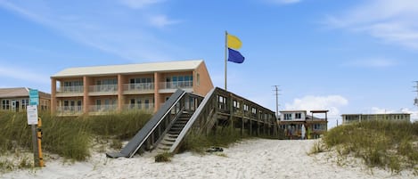 Un bâtiment situé en bord de mer, doté d’un escalier menant à un balcon, d’un drapeau et d’une enseigne indiquant qu’il se trouve en bord de plage.