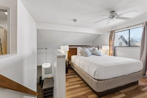 Quarto com cama, mesas de cabeceira, ventilador de teto e janela com cortinas.