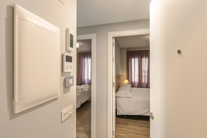 A hotel room with a bed, a bedside table with a lamp, a wall-mounted thermostat, and a door leading to another room. - A2 Apartment with Cathedral Views – Historic Center of Seville and Pool (Seville)
