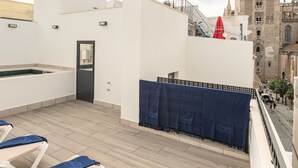 Terraza en la azotea con sillones de descanso y piscina, con vistas a una torre histórica.