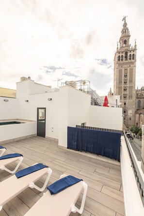Eine Dachterrasse mit Liegestühlen und einem Pool mit Blick auf einen historischen Turm.