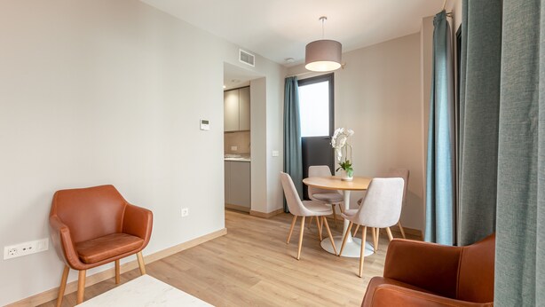 Una sala de estar moderna con comedor, con sillones de cuero, una mesa redonda y un gran ventanal con cortinas.