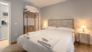 Habitación de hotel con cama, mesita de noche con lámpara, armario y calentador de pared.
