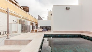 Zona de piscina con cerramiento de vidrio, una tumbona y una mesita.