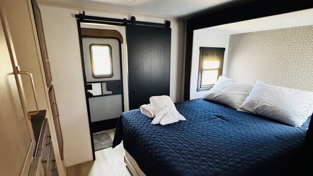 A bedroom with a bed, a window, and a door leading to a bathroom. - 2-bedroom recreational vehicle in lovely Exeter with AC (Exeter)