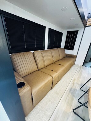 Ein modernes Interieur mit einem beige farbenen Sofa, schwarzen Jalousien und einem hellen Boden.