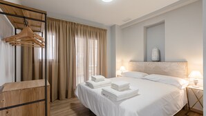 Een hotelkamer met een houten garderobe, een bed met witte lakens, een nachtkastje met een lamp en een raam met gordijnen.